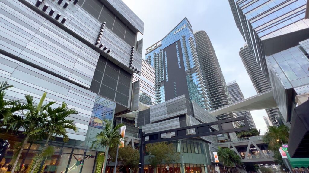 Street-level view looking up at glass high-rise towers above shops in Brickell, Miami