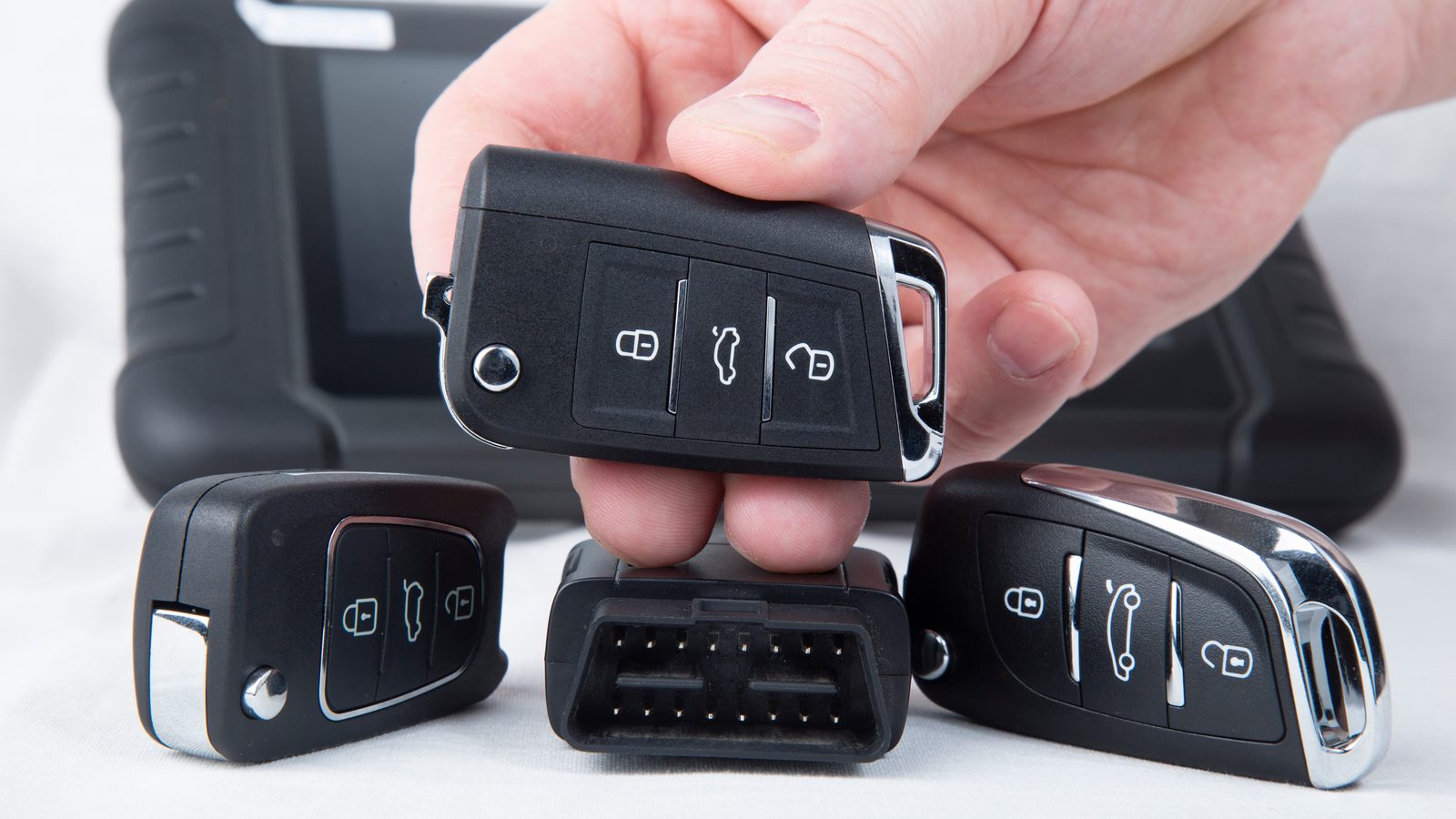Locksmith holding a replacement car key fob beside other key fobs and a key programming tool for lost car keys in Miami