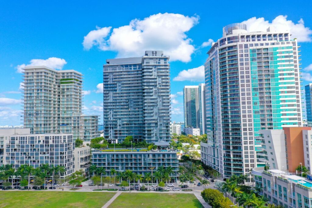 Condo and apartment towers in Midtown Miami seen from above a park, with palm-lined streets below